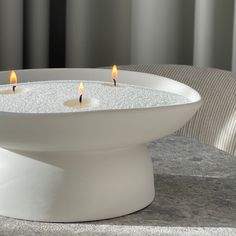 three lit candles in a white bowl on a table