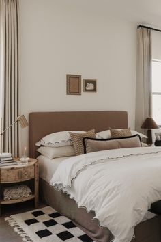 a bed with white sheets and pillows in a bedroom next to a window filled with curtains