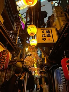 people are walking down an alley way with lanterns hanging from the ceiling and signs above them