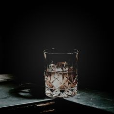 a shot glass with ice cubes in it sitting on a countertop next to a black background