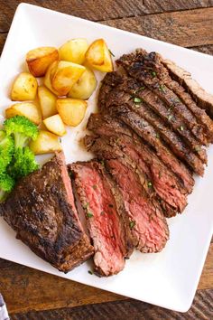 steak, potatoes and broccoli are on a white plate with a wooden table