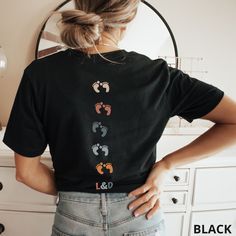 a woman standing in front of a mirror wearing a black shirt with footprints on it