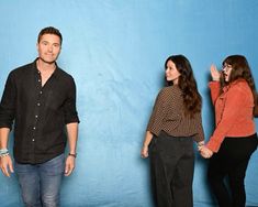 three people standing in front of a blue backdrop with one person holding his hand up