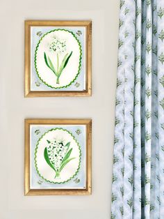 two framed pictures hang on the wall next to a window with blue and green curtains