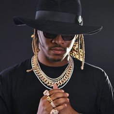 a man in a black hat and sunglasses with his hands clasped to his chest, wearing gold jewelry