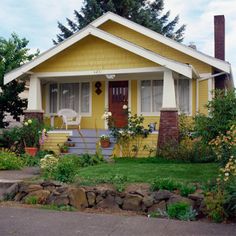 a yellow house with white trim and flowers in the front yard