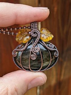 a hand holding a wire wrapped pendant with yellow beads on it's end and an orange bead around the clasp