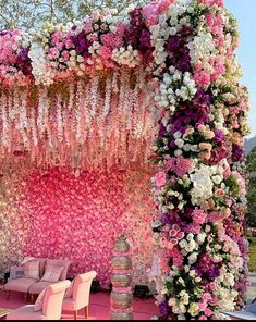 an outdoor wedding setup with pink and white flowers on the wall, couches and tables