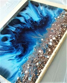 an abstract painting with blue and brown colors on it's surface, in a white frame