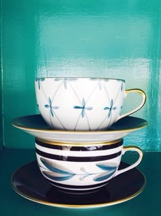 two cups and saucers sitting side by side on top of each other in front of a green wall