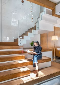 a woman sitting on the stairs reading a book in her living room, with sunlight streaming through the windows