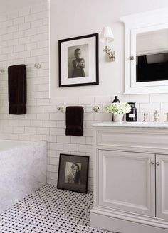 a white bathroom with black and white flooring, framed pictures on the wall above the bathtub