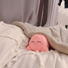 a pink stuffed animal laying on top of a white bed covered in blankets and pillows