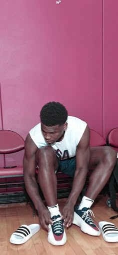 a man sitting on the floor tying his shoes in front of a pink wall with chairs behind him