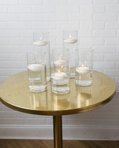 four candles are placed on a table with clear glass vases in front of them