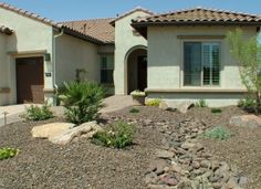 a house that has rocks and plants in the front yard with bushes on either side