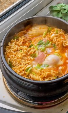 a pot filled with noodles and vegetables on top of a stove next to a window