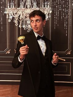 a young man in a tuxedo holding a flower and looking at the camera