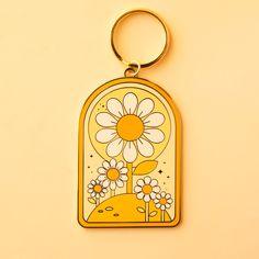 On a yellow background is an arched keychain with a gold loop and a white and yellow daisy design. Daisy Keychain, Beach Culture, California Beach, Much Needed, Fun Loving, Bits And Bobs, Playful Design, Original Design, Keychains