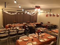 a room filled with tables and chairs covered in orange tablecloths, plates and silverware