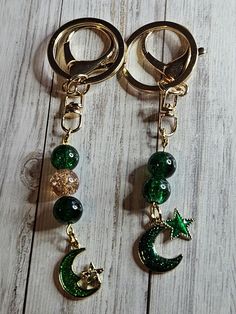 two key chains with charms attached to them on a wooden surface, one is green and the other is gold