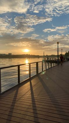 the sun is setting over the water and people are walking on the boardwalk by the water