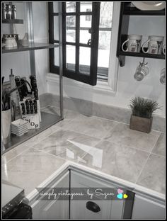 a kitchen with white marble counter tops and gray tile flooring, along with black framed windows