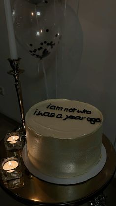 a white cake sitting on top of a table next to two candles and a balloon