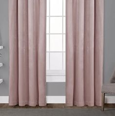 a pink curtain hanging on the side of a window next to a chair and shelf