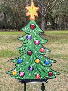 a large green christmas tree sitting on top of a metal stand in a park next to trees