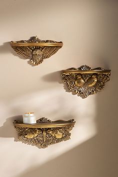 two gold wall mounted shelfs with candles on them and one holding a candle holder