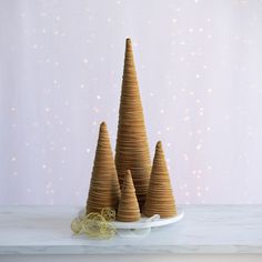 three small wooden christmas trees on a white plate with gold ribbon and lights in the background