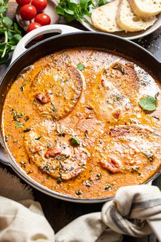 a pan filled with food on top of a wooden table next to bread and tomatoes