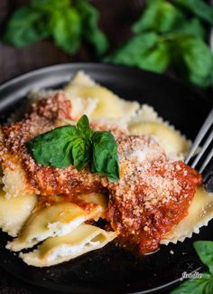 a black plate topped with lasagna sauce and basil garnished with parmesan cheese