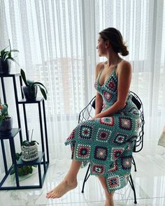 a woman in a crocheted dress sits on a chair and looks out the window