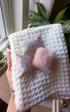 a person holding up a white blanket with two pillows on it and a pink pom - pom