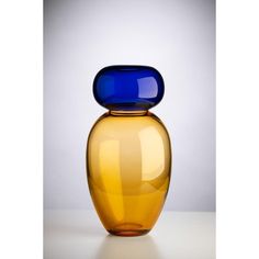 a blue and yellow glass vase sitting on top of a white table next to a gray wall