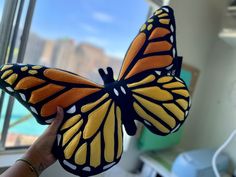 a hand holding a stuffed butterfly in front of a window