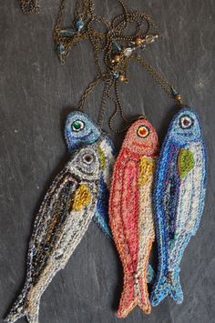 three fish are hanging from a chain on a black surface with beads and chains around them