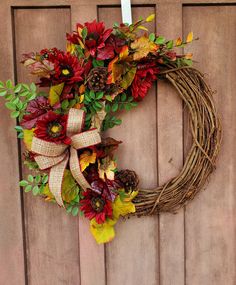 a wreath with fall leaves and pine cones hanging on a wooden door, ready to be decorated