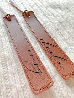 two leather tags with writing on them sitting on top of a white blanket next to a pair of scissors