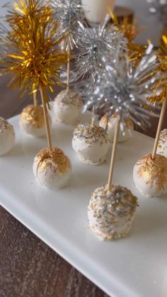 cake pops with gold sprinkles and sparklers on a white platter