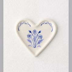 a heart shaped dish with blue and white flowers painted on it's side, against a white background