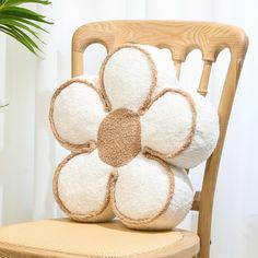 a white flower pillow sitting on top of a wooden chair next to a potted plant