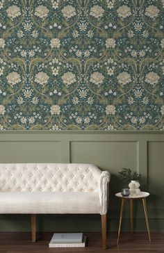 a white couch sitting in front of a green wall with flowers on it and a side table next to it