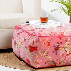 a pink flowered ottoman with a drink on it and a potted plant in the corner