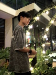 a young man standing in front of a building with plants and lights on the ground