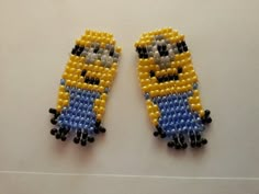 two yellow and blue beaded bird earrings sitting on top of a white table next to each other