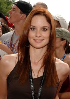 a woman with long red hair standing in front of a group of people at an event