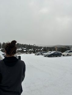 a woman standing in the snow looking at cars